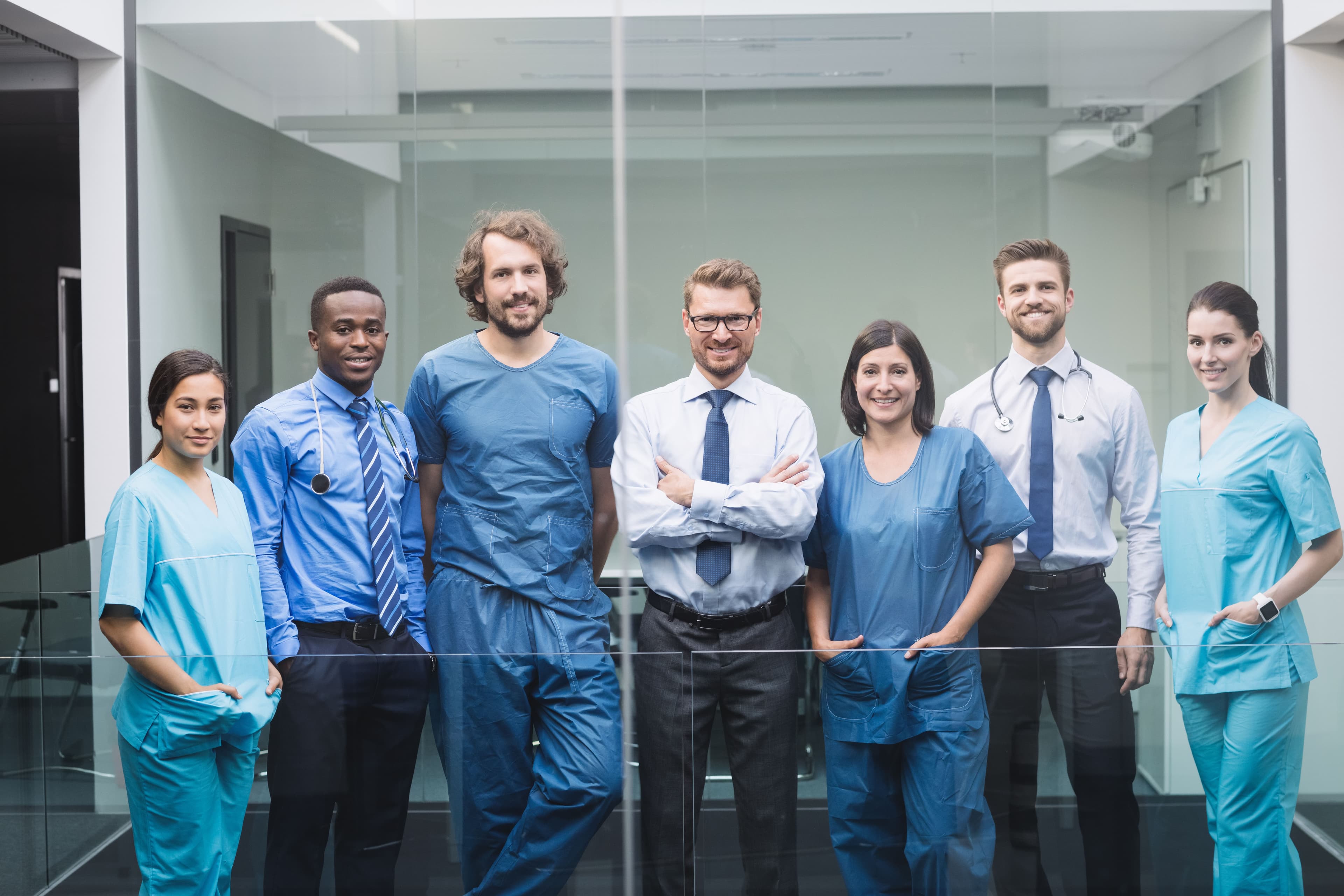 Seven doctors are smiling at corridor of hospital